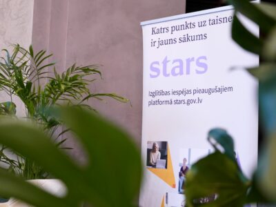 Balts stends ar tekstu "Katrs punkts uz taisnes ir jauns sākums", lieliem burtiem "stars" un "Izglītības iespējas pieaugušajiem platformā stars.gov.lv", redzams telpās starp zaļiem augiem.